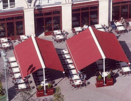 Store bannes rouges haut de gamme installés par Arca Menuiseries pour une terrasse de restaurant.