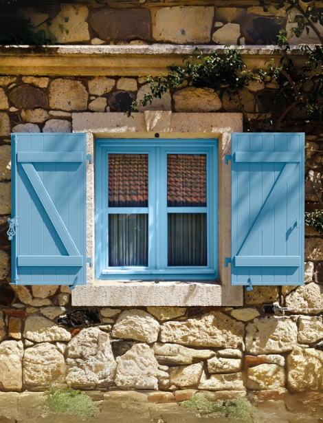 Fenêtre avec volets battants bleus en bois installés par Arca Menuiseries sur une maison en pierre.